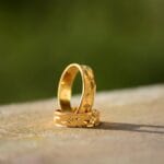 Close-up of two decorative gold wedding rings casting shadows on a warm surface.